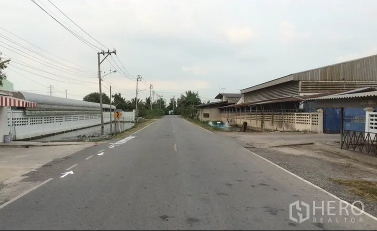 Warehouse for sale in Sai Noi, Nonthaburi - Quiet access road beside industrial properties and boundary walls with utility poles.