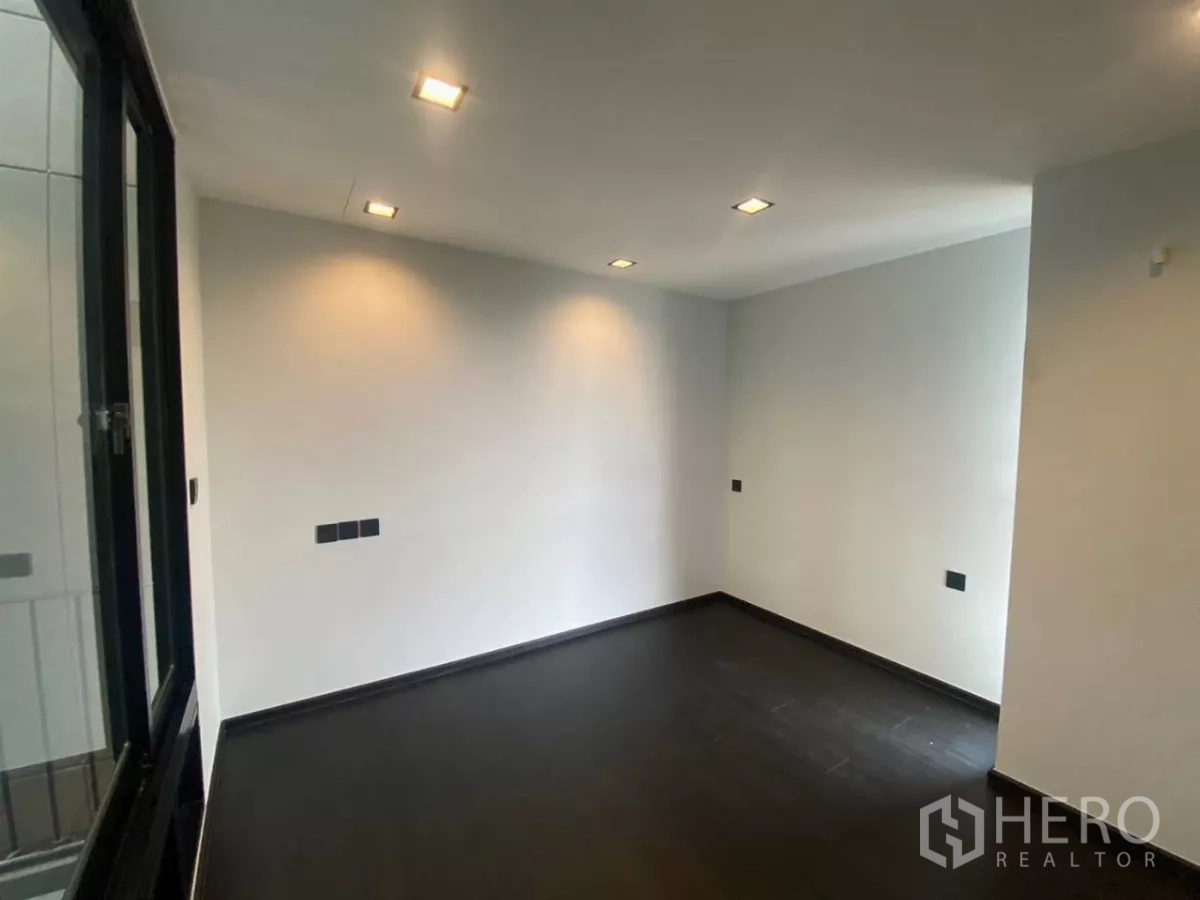 Townhouse for rent in Huai Khwang, Bangkok - Minimal bedroom with dark flooring and a large sliding window.