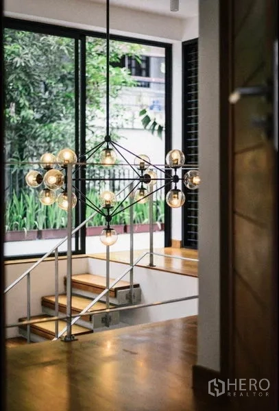 Townhouse for rent in Khlong Toei, Bangkok - Split-level staircase with statement chandelier beside a large garden-facing window.