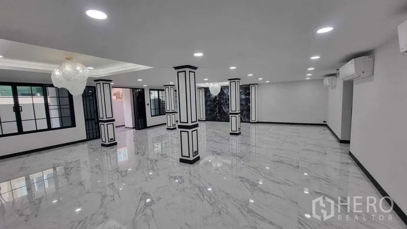 Townhouse for rent in Khlong Toei, Bangkok - Expansive open-plan living hall with marble-look tiles, decorative columns, and chandeliers.