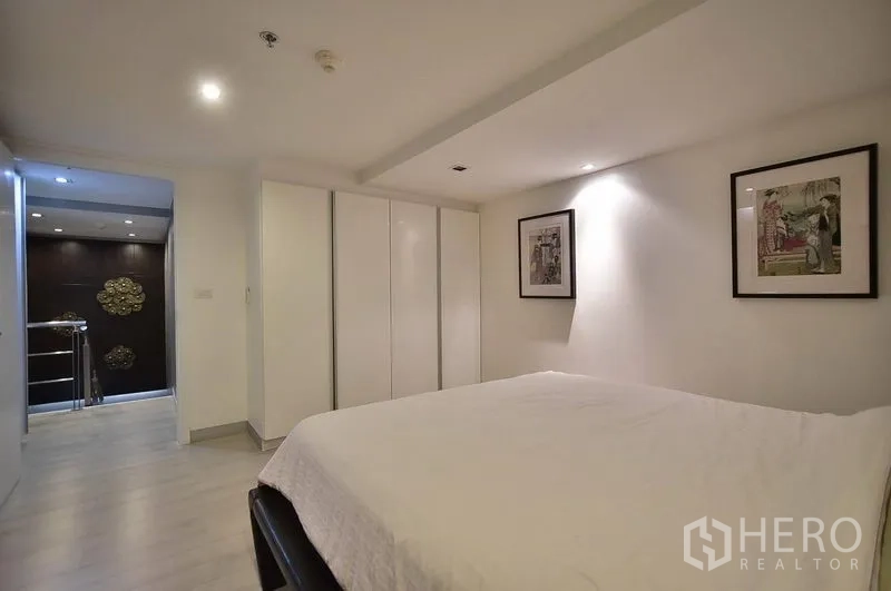 Condominium for rent in Khlong Toei, Bangkok - Cozy bedroom with built-in wardrobes and recessed lighting near the corridor.