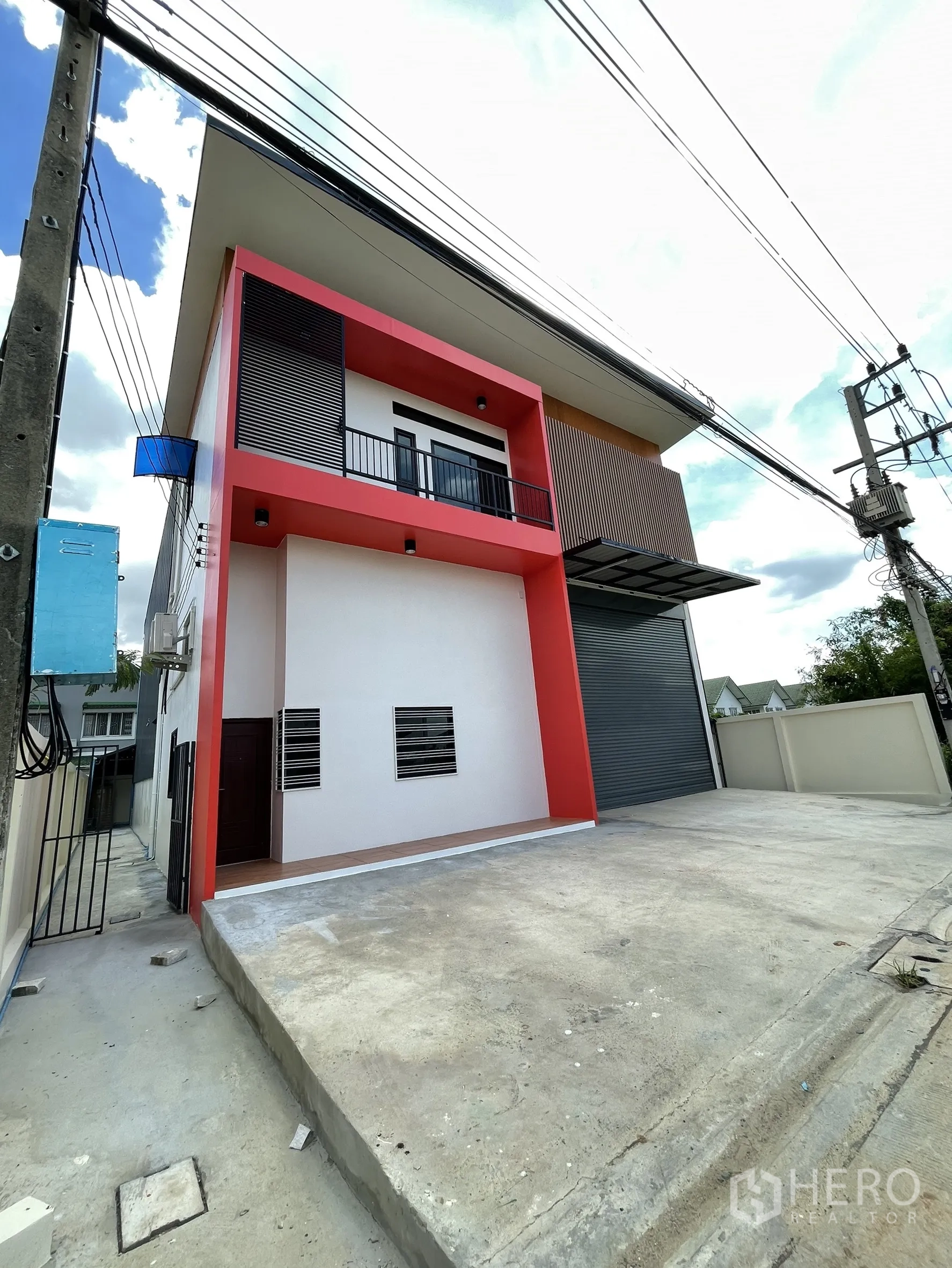 Factory for rent or sale in Lam Luk Ka, Pathum Thani - Angled front view showing the spacious concrete apron, balcony, and bold red exterior.