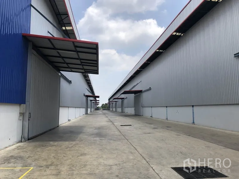 Factory for rent or sale in Phra Nakhon Si Ayutthaya - Wide concrete service lane between warehouses with multiple roller shutter doors.
