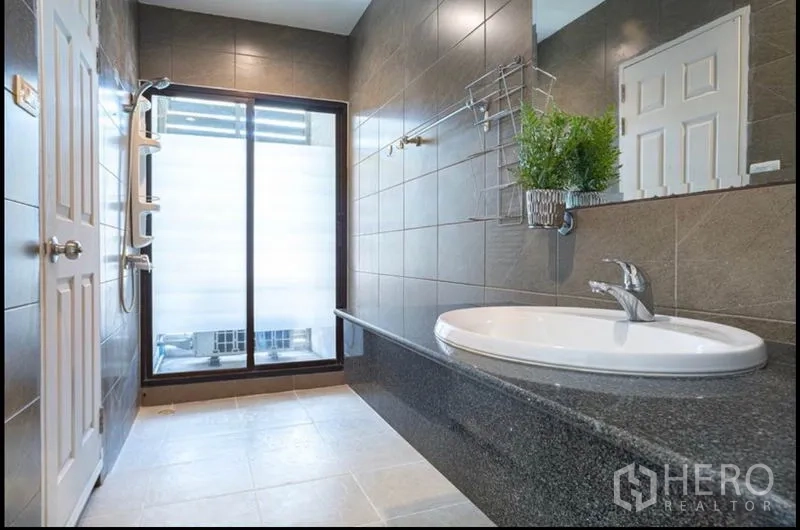Townhouse for sale in Khlong Toei, Bangkok - Contemporary bathroom with dark tiles, long granite vanity, rain shower and frosted glass door.