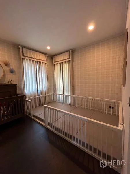Detached House for rent in Bang Kapi, Bangkok - Cozy child’s room with corner windows, soft wallpaper, and playpen area.
