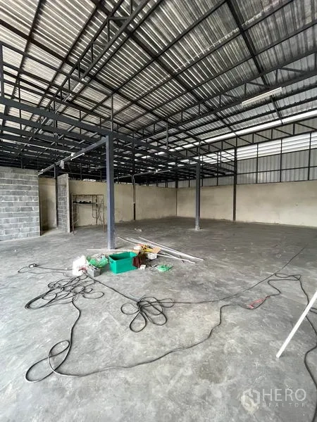 Warehouse for rent in Pathum Thani - Spacious warehouse floor with steel columns, block wall and electrical cables on the ground.