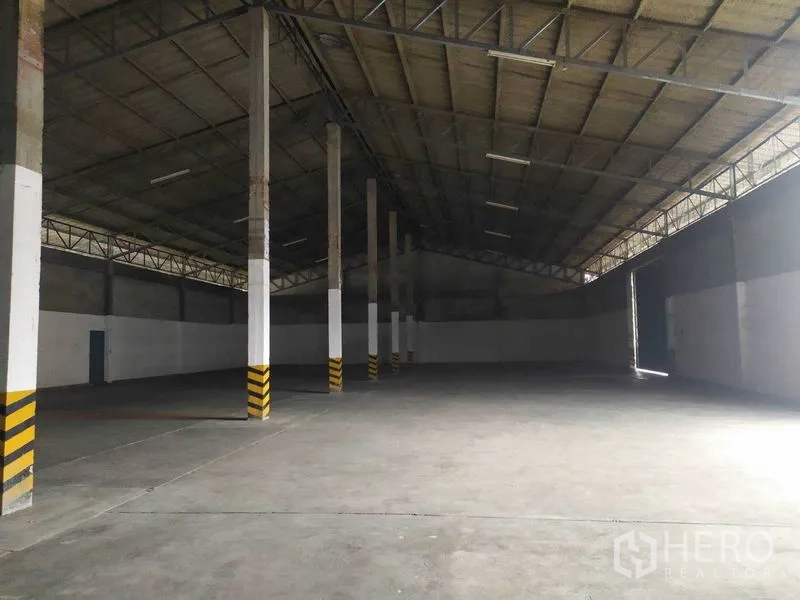 Warehouse for rent in Mueang Samut Prakan, Samut Prakan - Open warehouse bay showing tall columns, wide clear span and natural light near a large side door.