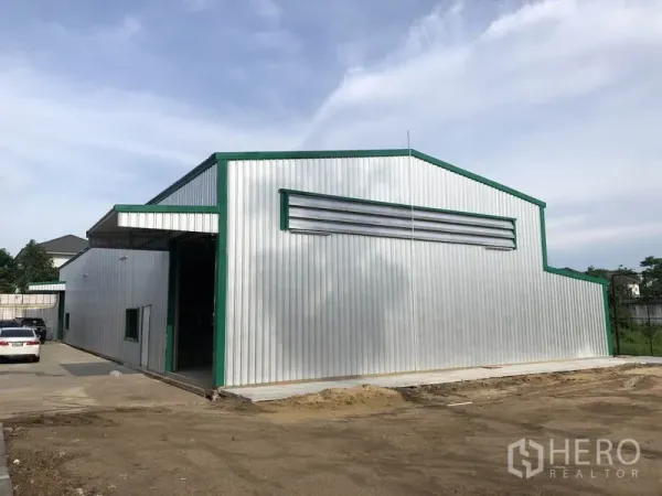 Warehouse for rent in Don Mueang, Bangkok - Corrugated metal warehouse exterior with green trim and a wide driveway for truck access.