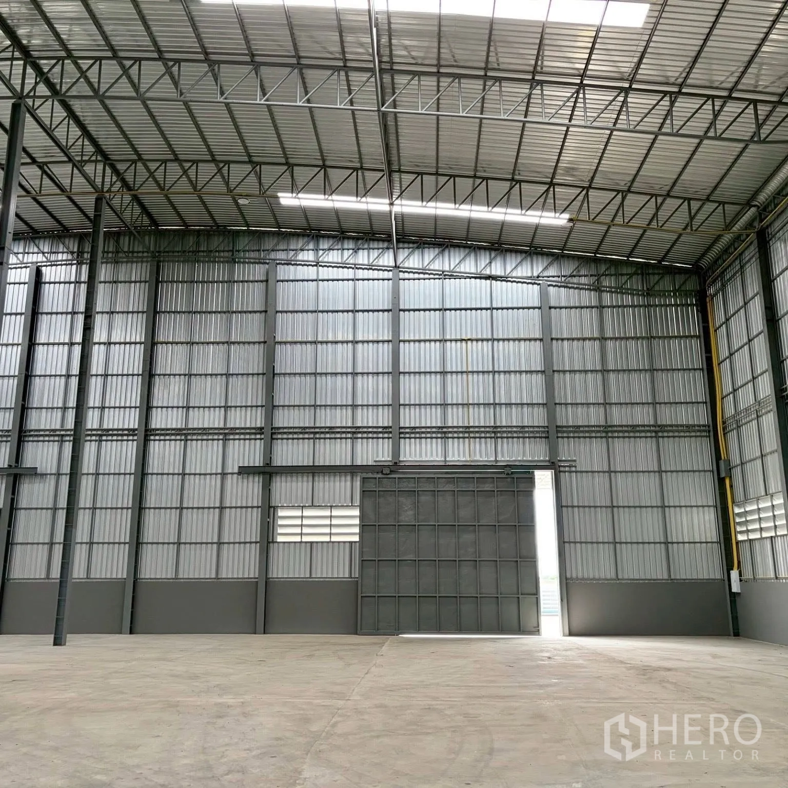 Factory for rent in Uthai, Phra Nakhon Si Ayutthaya - High-clear warehouse hall with steel trusses, skylights, and a large sliding door.