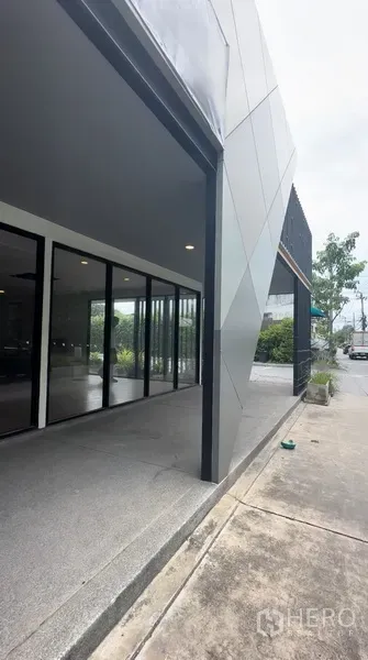 Retail Space for rent in Bang Na, Bangkok - Covered entrance of the retail space with floor-to-ceiling glass and angled metal panels along the street.