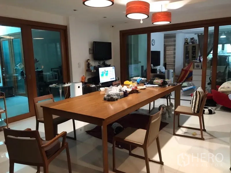 Detached House for sale in Lat Phrao, Bangkok - Dining room with long wooden table, pendant lights and sliding glass doors to adjacent living areas.