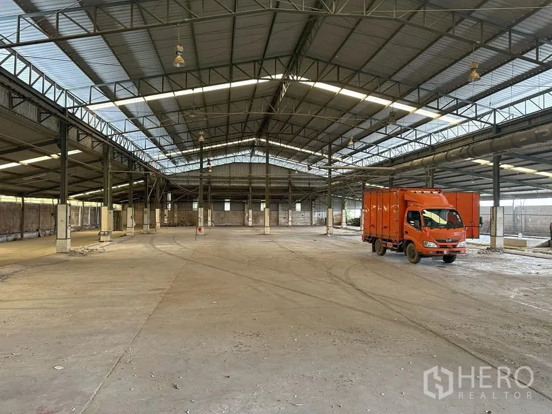 工厂 出租在Lat Lum Kaeo, Pathum Thani - 宽敞工厂内景，钢结构桁架屋顶与采光板，混凝土地面上有橙色卡车。