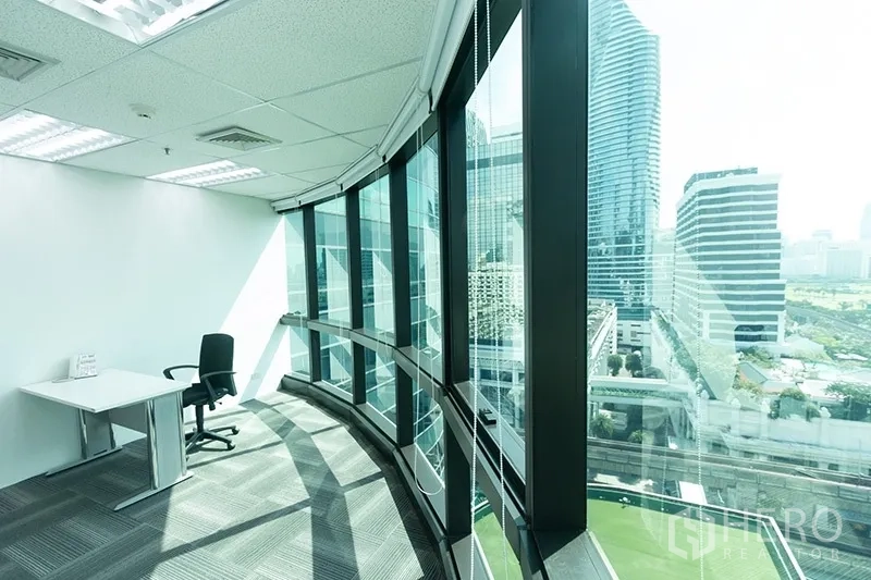 Office Space for rent - Private workstation along a curved glass facade with panoramic city views and abundant daylight.