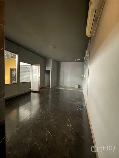 零售空间 出租 - 空置店铺空间，深色天花与黑色石地面，侧窗与玻璃门，墙挂空调。