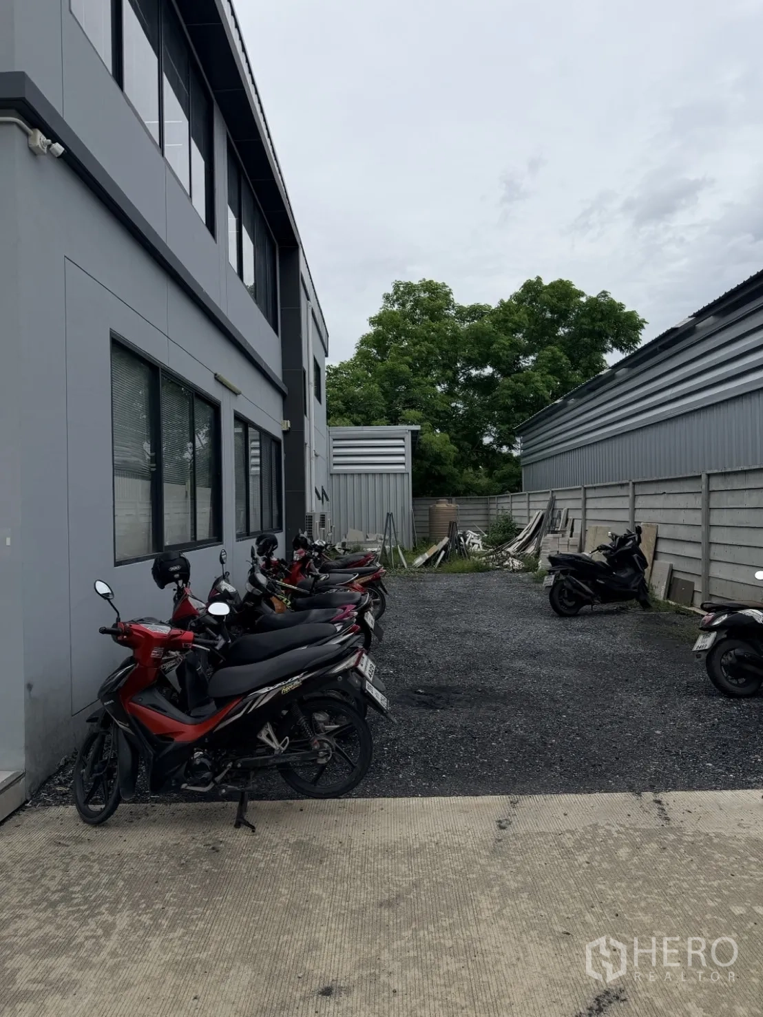 Factory for rent or sale in Lam Luk Ka, Pathum Thani - Exterior lane with grey office building and motorcycle parking.