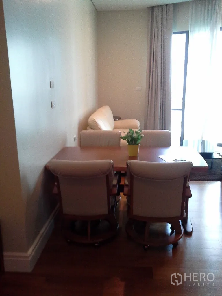 Condominium for rent or sale in Khlong Toei, Bangkok - Open living and dining area with armchairs, sofa, and a balcony door with sheer drapes.