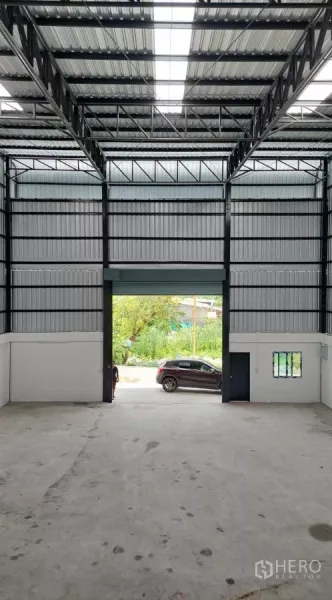 Warehouse for rent in Khlong Toei, Bangkok - Interior view toward the entrance showing tall steel trusses and a high roller door.