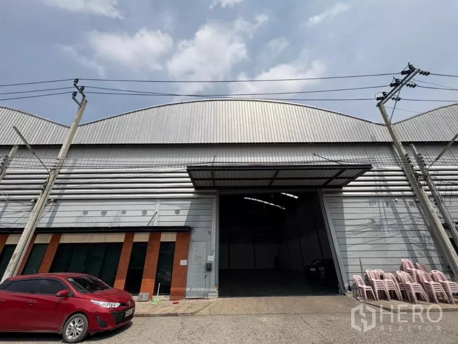 Warehouse for rent in Bang Phli, Samut Prakan - Street-side view of metal-clad warehouse facade with large roller shutter and parking in Bang Phli.