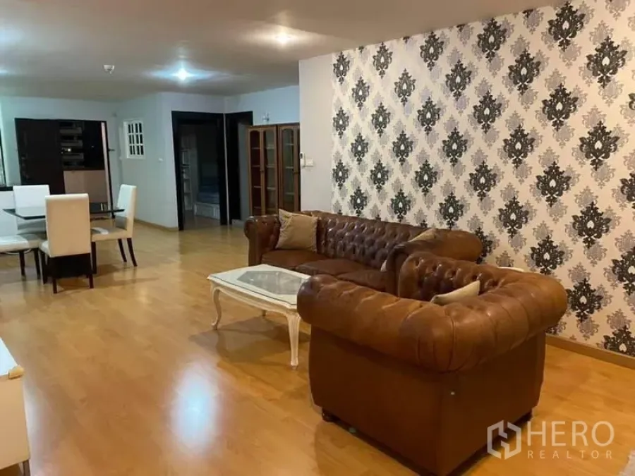 Condominium for rent or sale in Watthana, Bangkok - Open-plan living area with brown leather sofas, patterned feature wall, and wood flooring in a Bangkok condo.