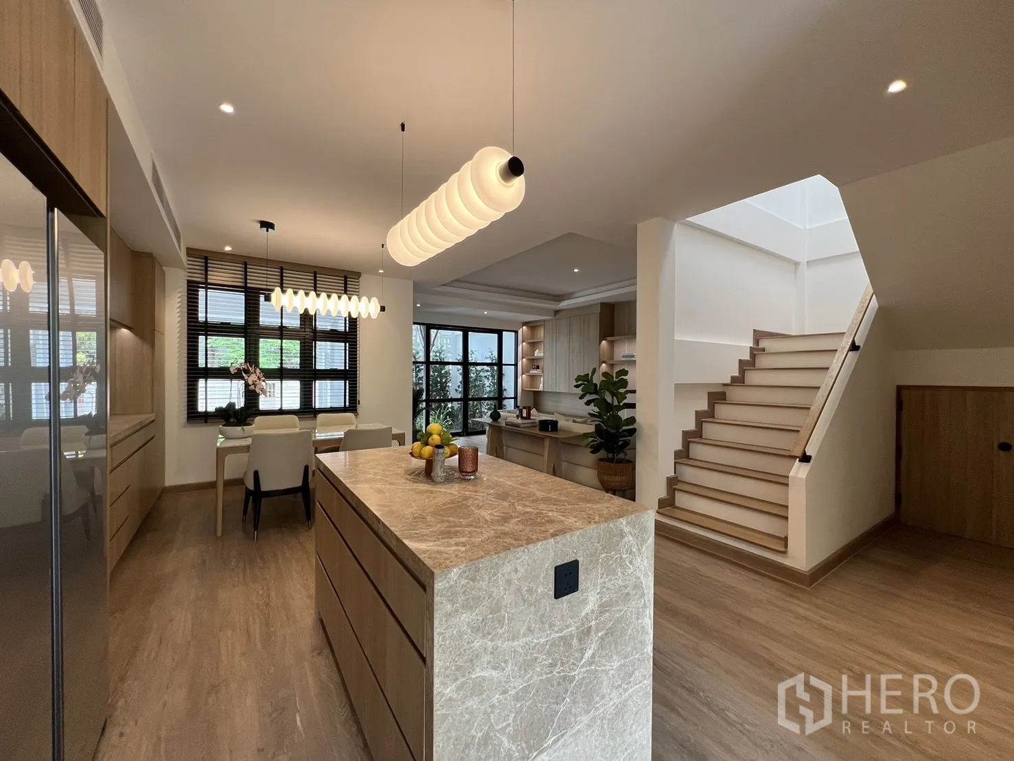 Townhouse for sale in Watthana, Bangkok - Kitchen and dining space with pendant lights next to a staircase and large windows.
