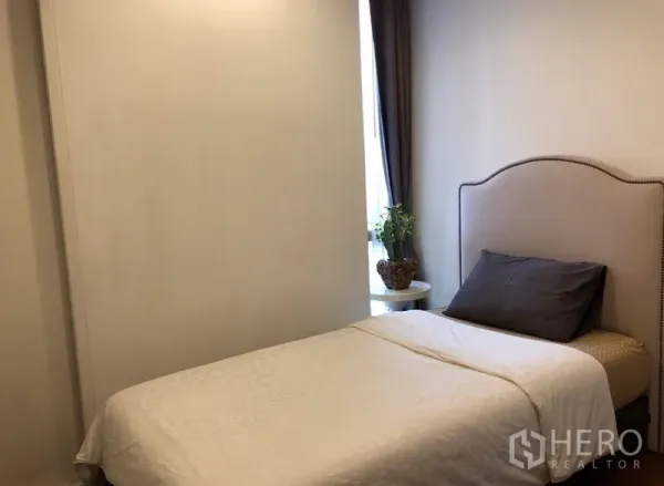 Condominium for rent in Khlong Toei, Bangkok - Cozy second bedroom with single bed, side table and natural light from a narrow window.