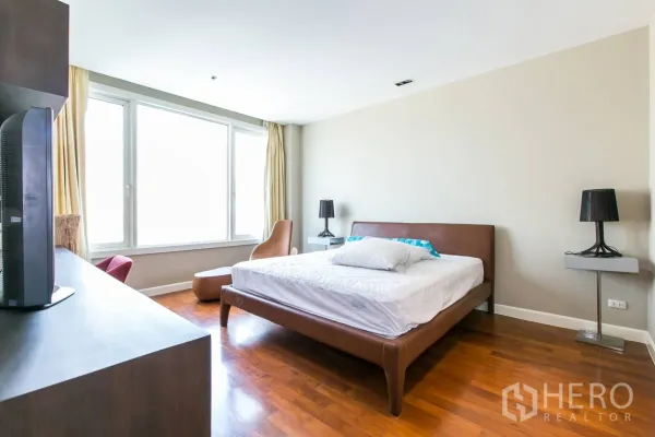 Condominium for rent or sale in Khlong Toei, Bangkok - Bright master bedroom with large window, leather bed, wood floors and lounge chair.