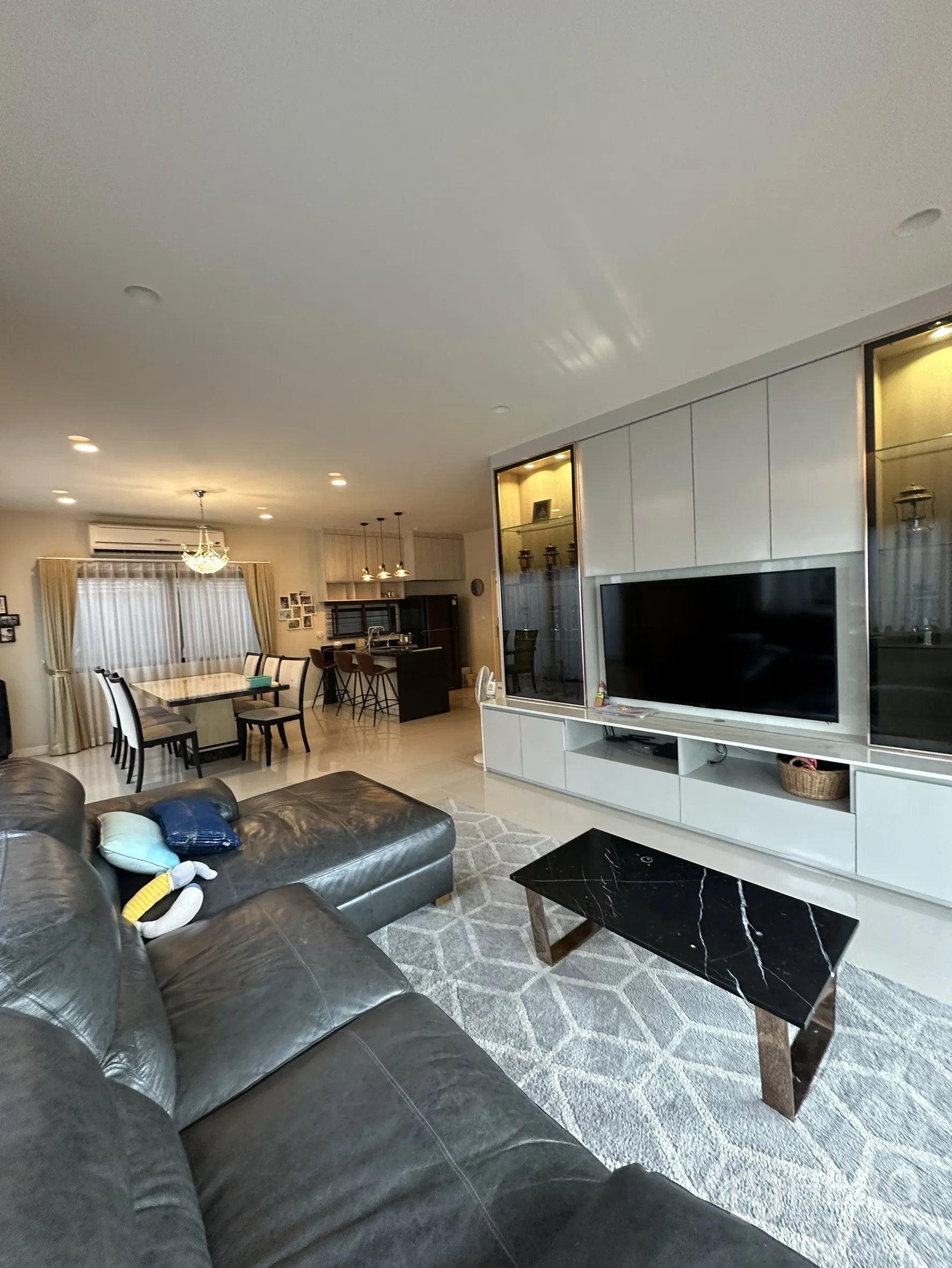 Detached House for rent or sale in Lam Luk Ka, Pathum Thani - Spacious open-plan living room with leather sectional, built-in TV wall and view to dining and kitchen.