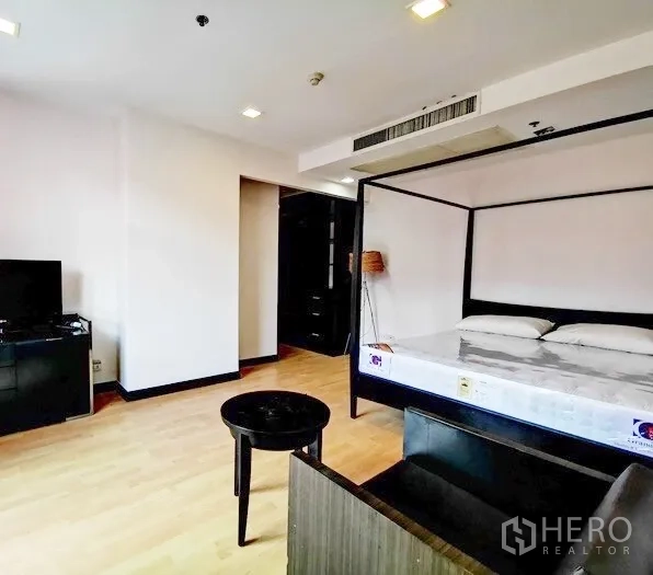 Condominium for rent in Khlong Toei, Bangkok - Spacious second bedroom with four‑poster bed, TV cabinet and wood floors.