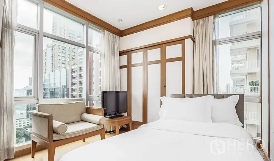 Condominium for rent in Pathum Wan, Bangkok - Corner bedroom with large windows, city view, double bed, wardrobe and TV.