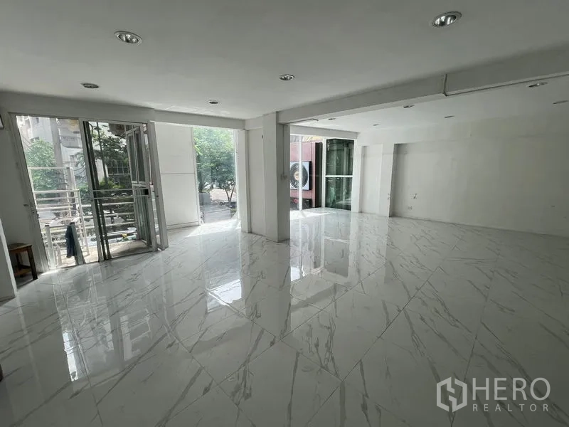 Retail Space for rent in Khlong Toei, Bangkok - Bright open-plan retail interior with large windows and glossy marble-look tiles opening to a small terrace.