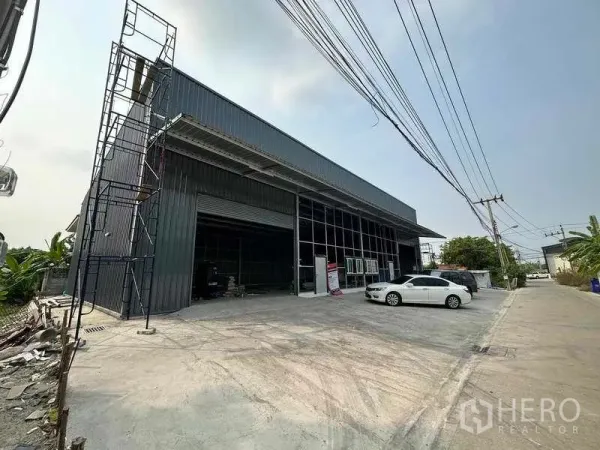 Warehouse for rent in Pak Kret, Nonthaburi - Angled view of the warehouse facade showing loading bay, tall canopy roof and broad driveway for truck access.