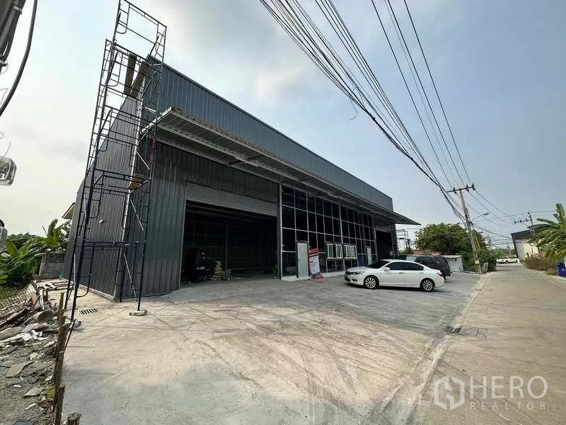 Warehouse for rent in Pak Kret, Nonthaburi - Angled view of the warehouse facade showing loading bay, tall canopy roof and broad driveway for truck access.