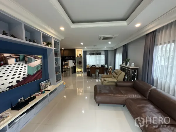 Detached House for rent in Lam Luk Ka, Pathum Thani - Long living area with TV feature wall, sofa and dining zone by windows.