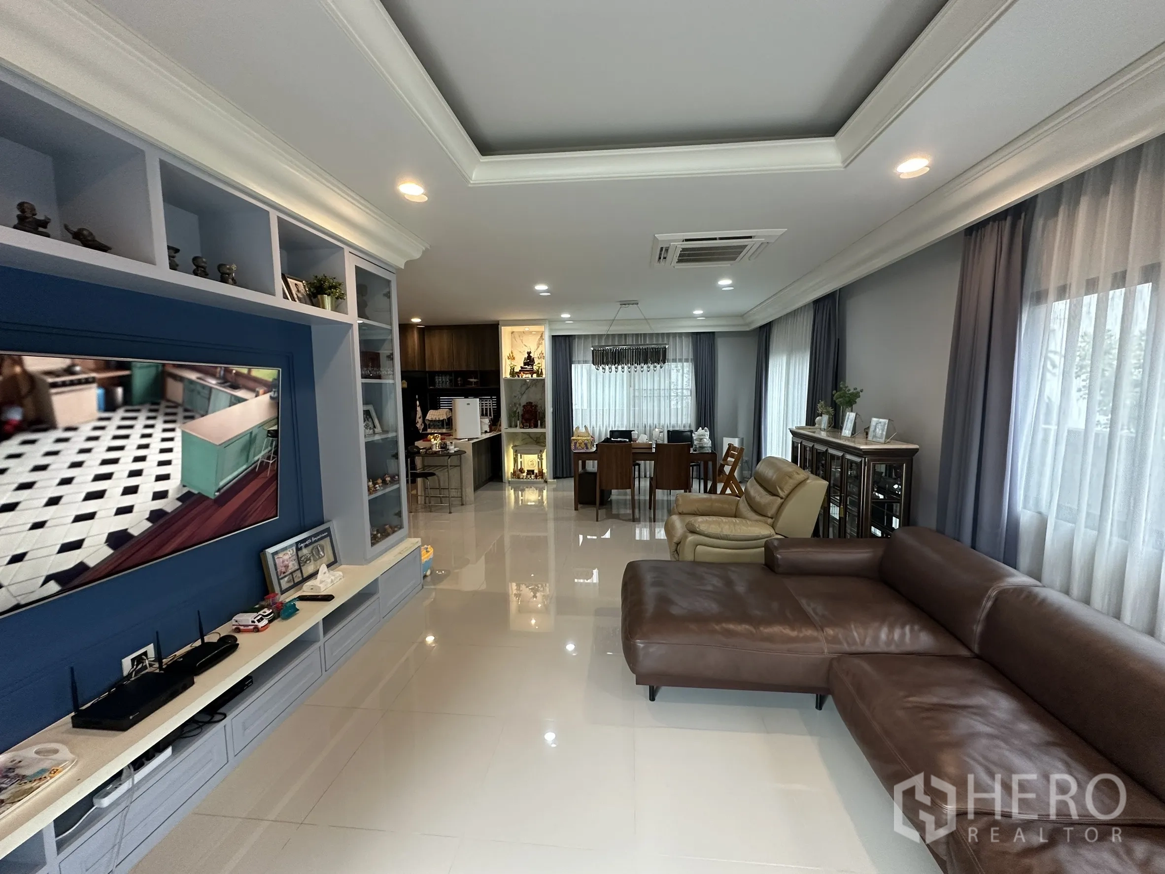 Detached House for rent in Lam Luk Ka, Pathum Thani - Long living area with TV feature wall, sofa and dining zone by windows.
