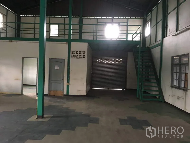 Warehouse for rent in Saphan Sung, Bangkok - Open-plan warehouse area with mezzanine, internal staircase, and roller-shutter loading door.