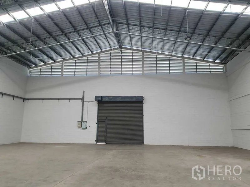 货栈 出租在Khlong Luang, Pathum Thani - 仓库端墙配大卷闸门、上部百叶窗与电力配电箱。