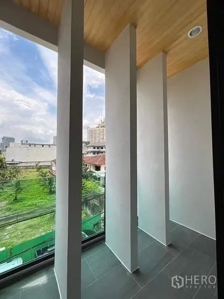 联排别墅 出售在Watthana, Bangkok - 狭长阳台，竖向遮板与玻璃栏杆，俯瞰社区绿地