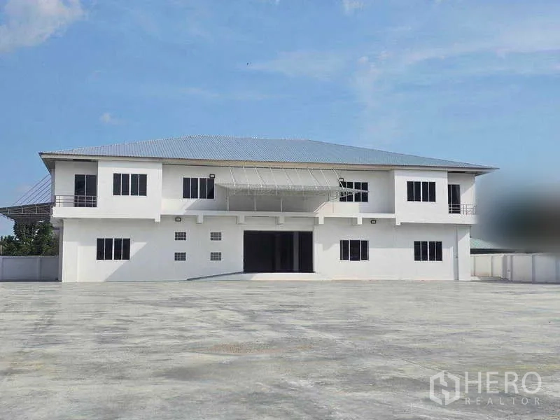 Warehouse for rent in Mueang Samut Prakan, Samut Prakan - Two-storey warehouse building with an expansive paved yard for truck parking.