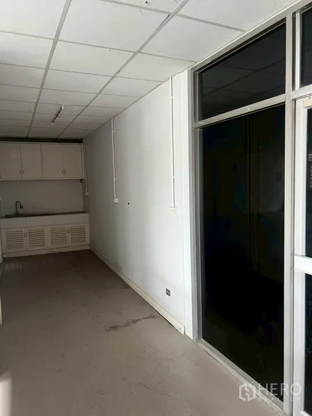 Shophouse for rent in Phra Khanong, Bangkok - Compact pantry with sink and upper cabinets beside a dark glass partition.