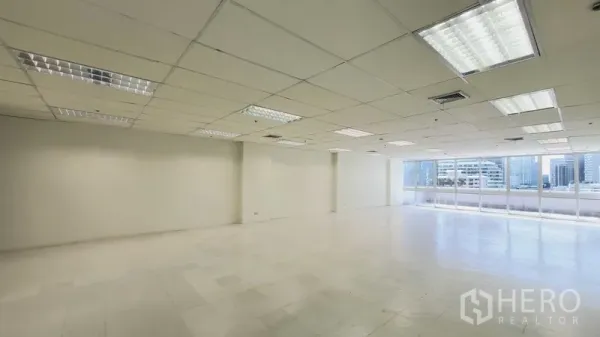 Office Space for rent in Khlong Toei, Bangkok - Corner view of an open office showing wide window wall and fluorescent lighting.