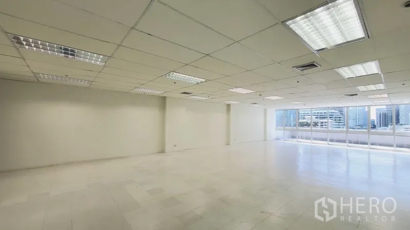 Office Space for rent in Khlong Toei, Bangkok - Corner view of an open office showing wide window wall and fluorescent lighting.