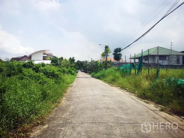 Warehouse for rent in Bang Khen, Bangkok - Concrete access road to the Bang Khen warehouse, lined with greenery and nearby houses.