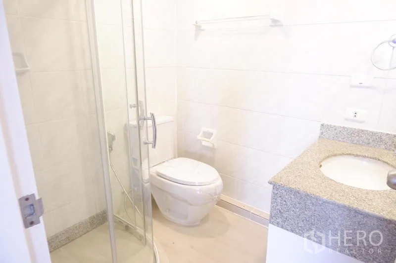 Condominium for rent in Khlong Toei, Bangkok - Bright bathroom with glass shower enclosure, toilet and granite-top vanity.