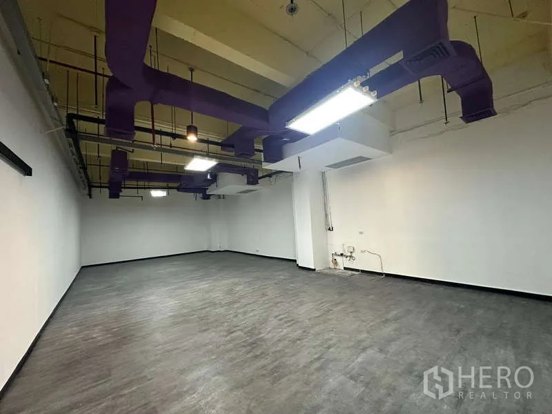 Office Space for rent - Open-plan office with high ceiling, exposed ductwork, suspended LED lighting and dark vinyl floors in Pathum Wan, Bangkok.