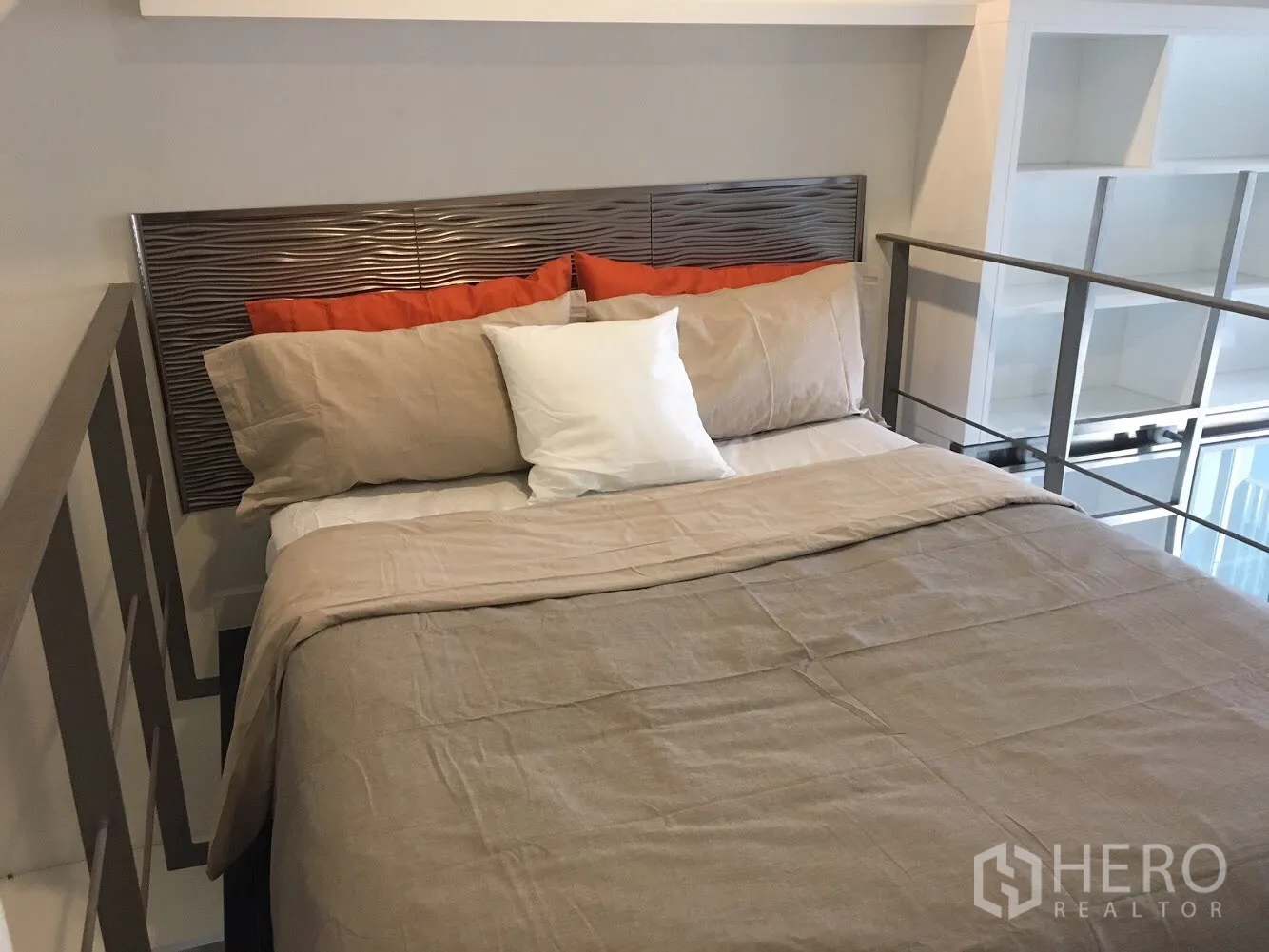 Condominium for rent in Khlong Toei, Bangkok - Loft-style bedroom with beige bedding, textured headboard, side railings and open shelving.