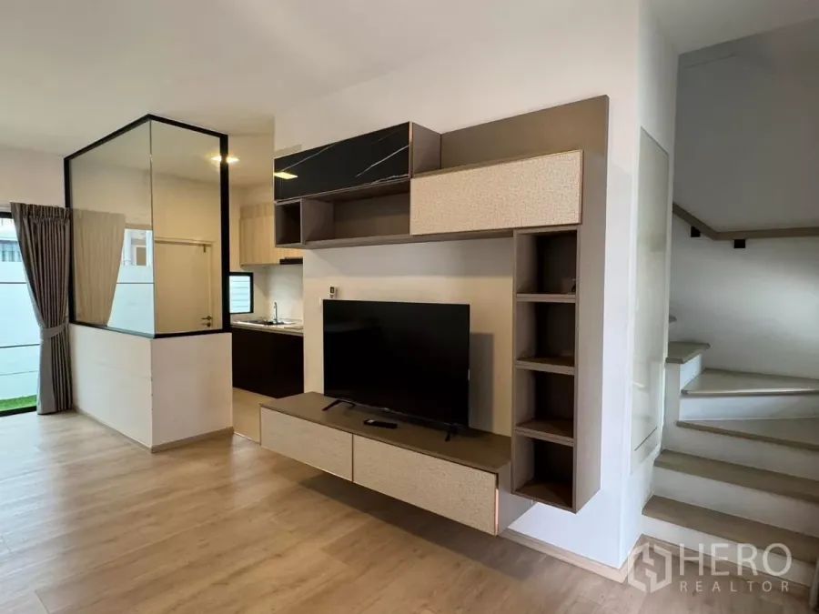 Townhouse for rent in Bang Phli, Samut Prakan - Bright living room with built-in TV wall, glass partition, and view to kitchen and stairs.