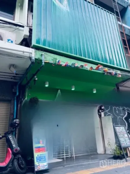 Shophouse for rent or sale in Khlong Toei, Bangkok - Multi-storey shophouse facade with green metal cladding and roll-up shutter along the sidewalk.