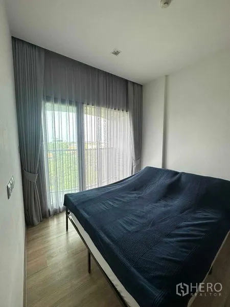 Condominium for sale in Watthana, Bangkok - Cozy bedroom with floor‑to‑ceiling window, sheer curtains, and wood flooring.