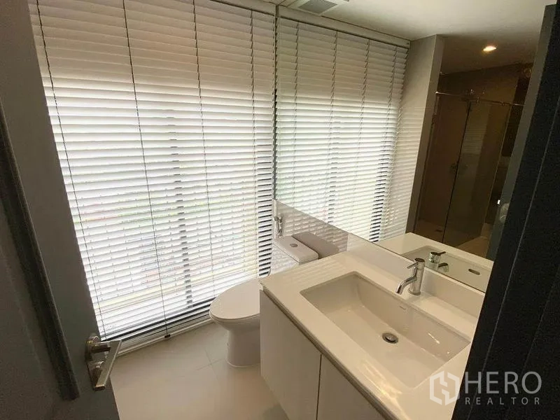 Condominium for rent in Pathum Wan, Bangkok - Bathroom with wide window blinds, white vanity, toilet and separate shower area.