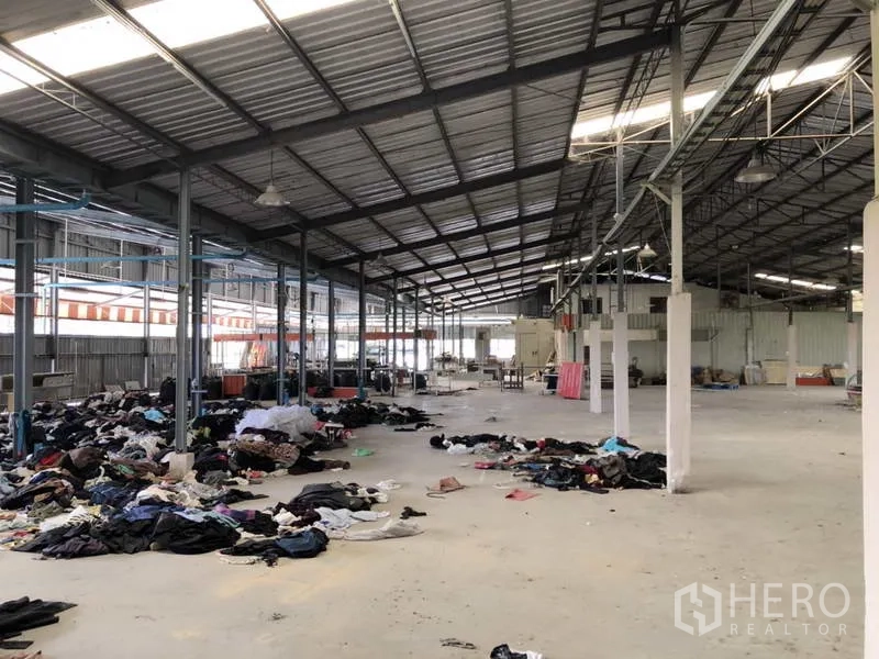 Warehouse for rent or sale in Khlong Luang, Pathum Thani - Expansive storage area with metal roofing, columns, and scattered materials on the floor.